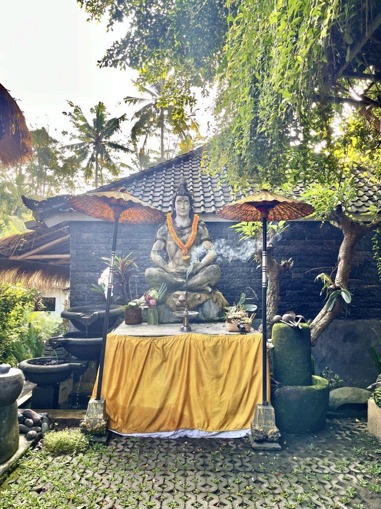 Balinese temple altar with meditating statue, incense, and offerings used for a sacred water ceremony in Bali