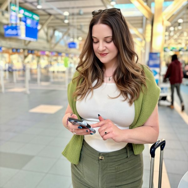 Woman entrepreneur at the airport using her phone beside her carry-on luggage, staying organized and productive while traveling