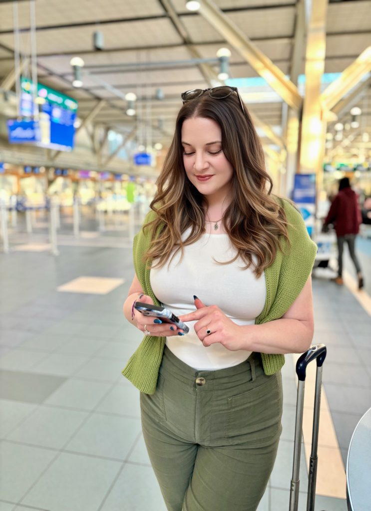 Woman entrepreneur at the airport using her phone beside her carry-on luggage, staying organized and productive while traveling