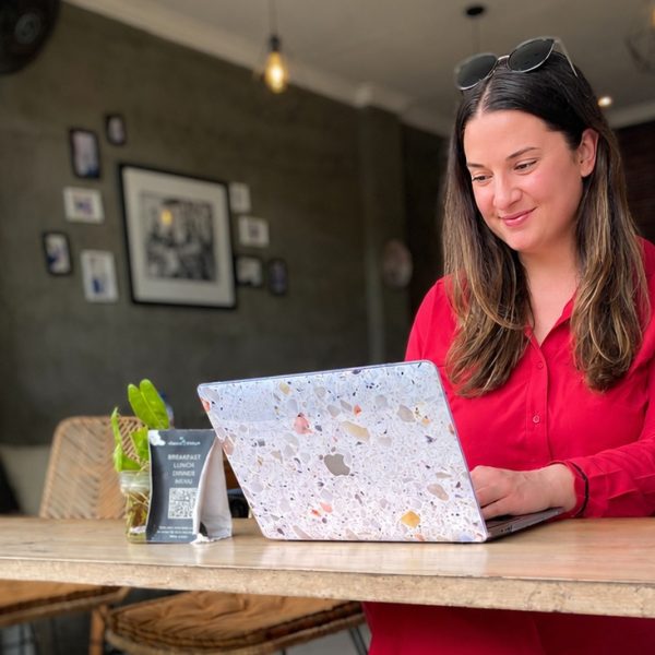 A woman entrepreneur working on her laptop at a wooden table in a lush, tropical cafe in Bali, surrounded by green plants and a peaceful atmosphere.